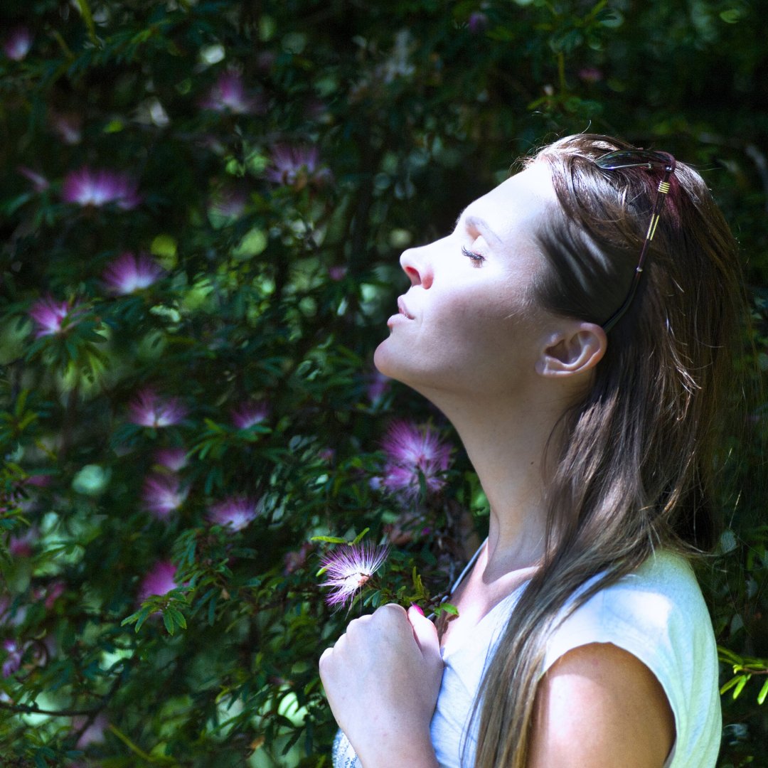 Jeune femme les yeux fermés, respirant au milieu de fleurs violettes